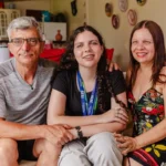 Adolescente apresentando projeto em feira de ciências acompanhada pelos pais