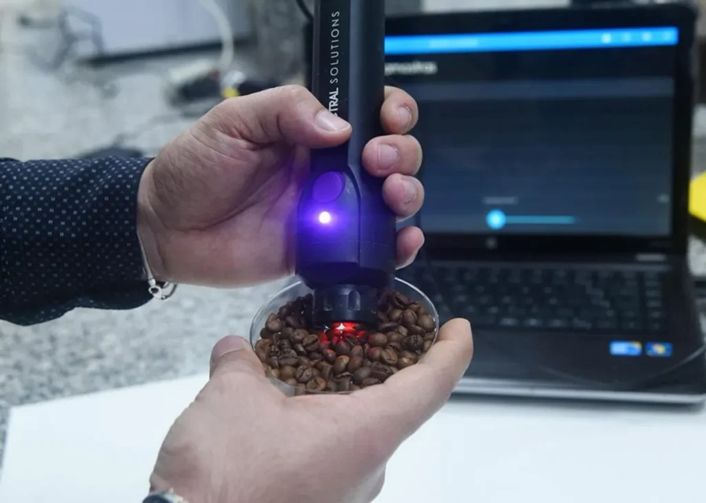 Pesquisador usando espectrômetro NIR portátil sobre grãos de café em bandeja