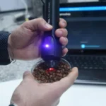 Pesquisador usando espectrômetro NIR portátil sobre grãos de café em bandeja