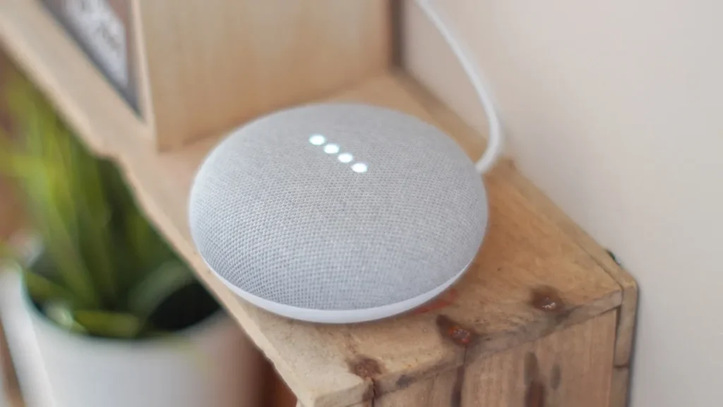 Google aceita pagar US$ 68 milhões em processo por espionagem de seu assistente virtual 1 Google Home Mini e smartphone mostrando onda sonora do assistente, com papéis judiciais ao fundo