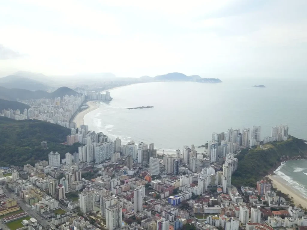 Fachada da prefeitura de Guarujá com dois agentes urbanos conversando e tablet mostrando gráficos digitais