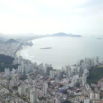 Fachada da prefeitura de Guarujá com dois agentes urbanos conversando e tablet mostrando gráficos digitais